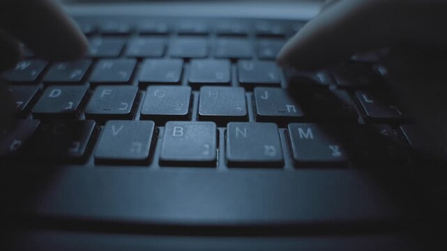 Hands typing fast on computer keyboard with Hebrew letters. Hacker or spy writing memo or sending information coding program software app. Dark web desk in office working late at night. Corporate