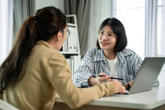 Two women collaborate at a desk with a laptop  , Scene is one of collaboration and communication`