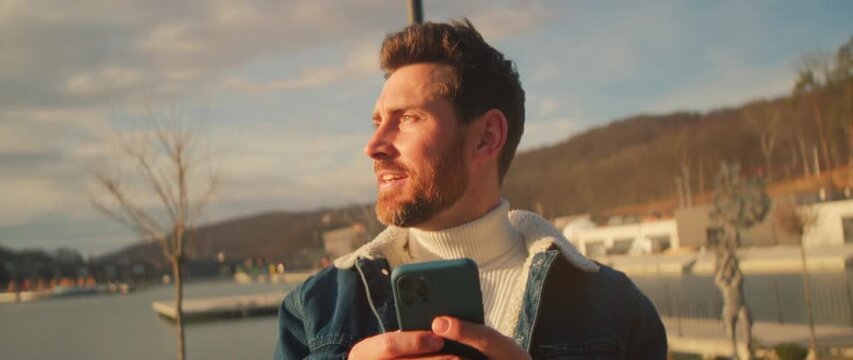 Casual man smiling by harbor, Man dressed in casual clothing smiling at his phone near tranquil harbor setting