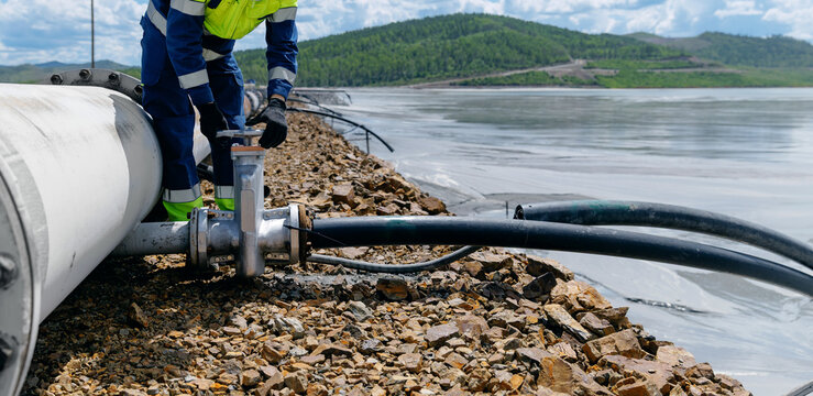 Worker operating valve on pipeline at Copper, iron ore mining industry sludge ponds, tailings storage facilities