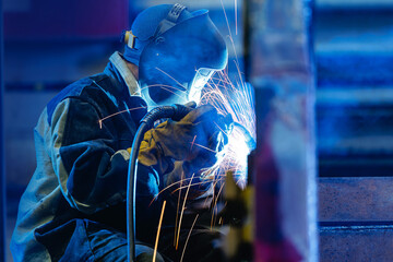 Welder operating arc welder producing sparks in workshop, recovery work for excavator bucket © Parilov