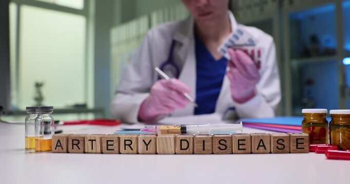 Wooden blocks spell phrase Artery Disease by vials and tablets. Doctor measures sample noting key risk factors for cardiovascular treatment of patient
