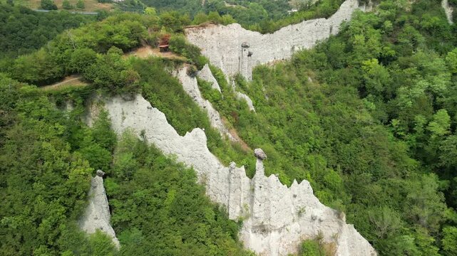 Drone fly in toward hoodoo pillars at Zone near Lake Iseo Lombardy Italy, drone glides past jagged gray spires and reveals sandy walls cut into green slopes