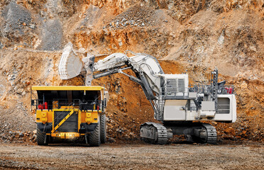 Mining work, Big Excavator loading gold, copper and iron ore into haul yellow truck at open pit quarry © Parilov