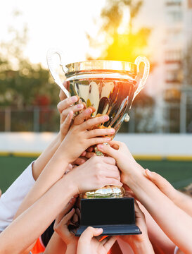Girls youth football team celebrating victory with trophy at sunset, winner cup