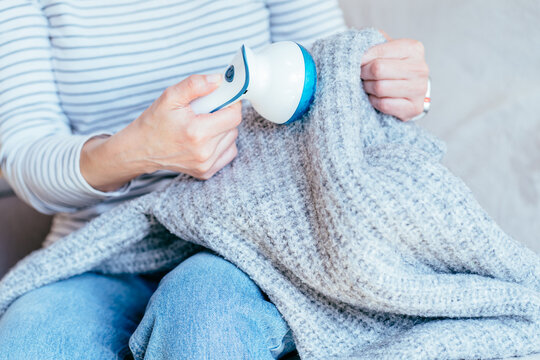 Woman cleaning gray knit blanket with fabric shaver while sitting at home