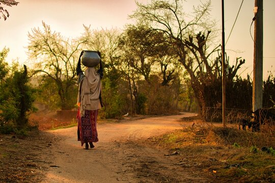 young rural woman walking on the village path in the morning carrying a load on her head