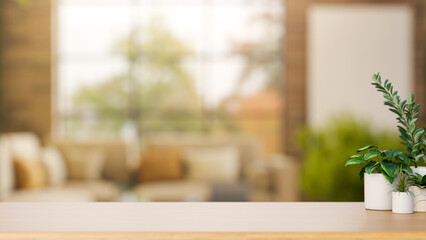 Fototapeta premium Potted plants on wooden counter table across sofa and glass window in a blurred living room or cafe.