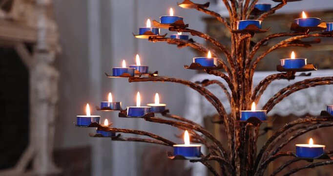 Tree shaped wrought iron candelabrum with lit blue candles, static shot shows branching holders and steady flames while a soft baroque altar background stays blurred in warm candle light