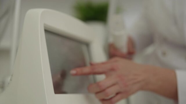 Cosmetologist preparing microneedling machine for antiaging radiofrequency skin treatment, selecting settings on touchscreen for beauty procedure in clinic. Concept of beauty, facial anti-aging.