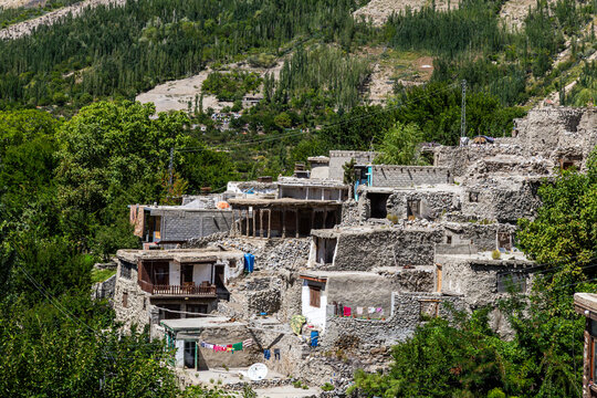Aerial view of stone and mud houses nestled amid lush greenery, with the majestic mountains looming in the background, Hunza Nagar, Gilgit, Pakistan.