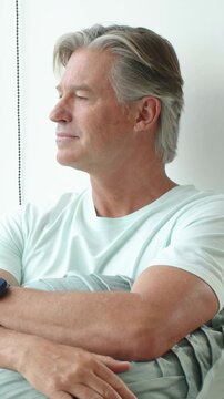 Vertical video: Sunlight nudging man opening eyes, gazing at window in mint tee and tapping cushion