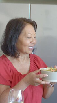 Vertical video: Holding woman in red blouse savoring bowl aroma after offscreen comment in kitchen