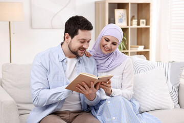 Fototapeta premium Happy muslim couple reading book on sofa at home