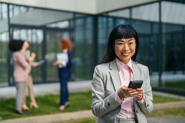 Fototapeta premium Asian businesswoman using smart phone outside modern office building