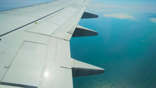 Airplane flying above calm blue sea with wing flaps visible. Jet cruising over ocean waters with wing structure in frame. Passenger aircraft gliding across marine horizon showing wing panels