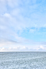 Fototapeta premium Landscape, farmland and sky with snow in nature for agriculture, dormant crops and winter season. Space, clouds and climate change with frost for soil moisture, rural farming and planting disruption