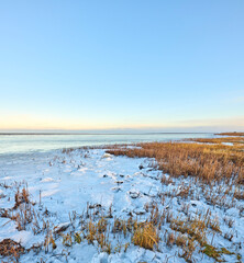 Fototapeta premium Landscape, grassland and beach with snow in nature for climate change, winter season and morning frost. Space, blue sky and seaside with ice formation, snowfall and icy conditions from global warning