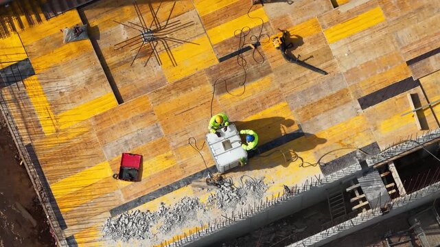 Aerial drone shot looking straight down at two construction workers installing steel reinforcement on formwork deck, showcasing structural preparation and active building process.