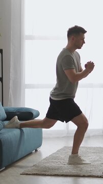 Young man performing Bulgarian split squat exercise at home using sofa support, demonstrating balance, strength training, and functional lower body workout routine