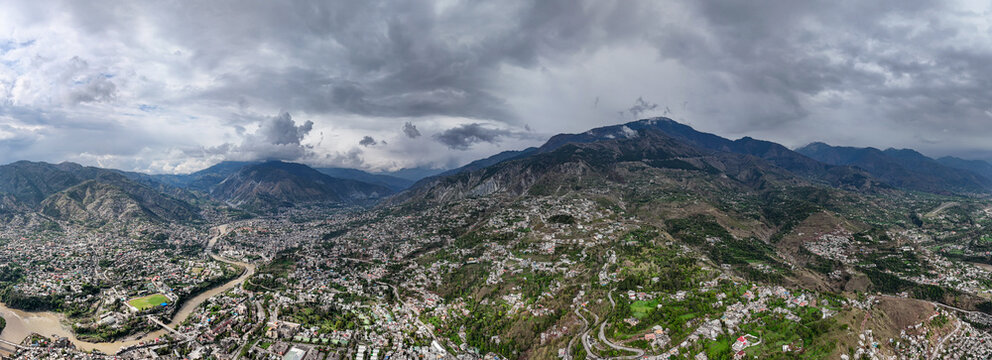 Aerial view of a city nestled between rolling hills, with the river snaking through, under a dramatic sky, Muzaffarabad, Azad Kashmir, Pakistan.
