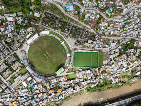 Aerial view of the vivid green cricket ground and adjacent hockey field stand out amidst the dense urban sprawl, Muzaffarabad, Azad Kashmir, Pakistan.
