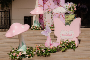 Obraz premium Enchanting outdoor whimsical party decorations featuring pink mushrooms, delicate butterflies, and lush floral arrangements on wooden steps in natural light