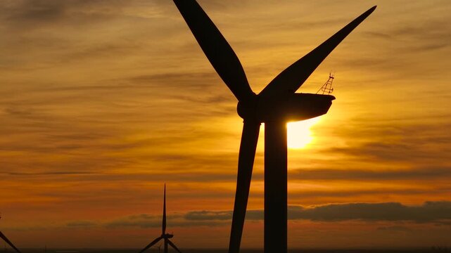 Windmill turning in glowing sunset breeze. Creating energy from warm wind flow. Generating renewable power with rotating blades. Delivering clean electricity using environmental force