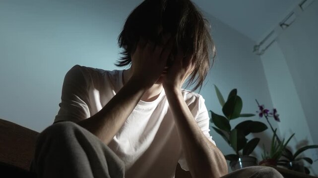 Young man covering face with hands feeling deep despair and overwhelming depression. Person leaning forward experiencing emotional breakdown and intense inner tension. Teenager hiding face showing
