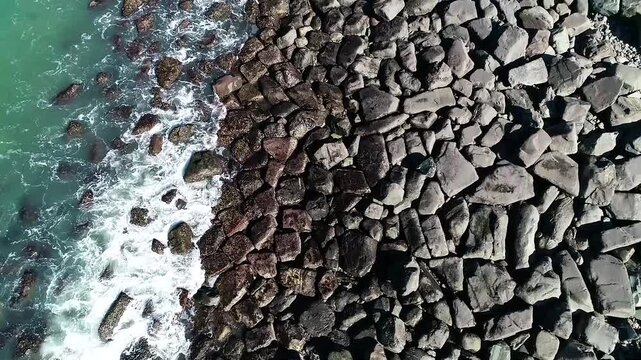 Cinematic aerial top view forward tracking shot over rocky coastline with waves creating natural texture and abstract ocean pattern for background use
