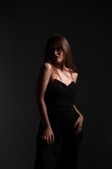 Fototapeta premium Elegant young woman wearing black strapless dress and stylish yellow tint glasses posing in dark studio, expressing confidence, fashion, and mystery