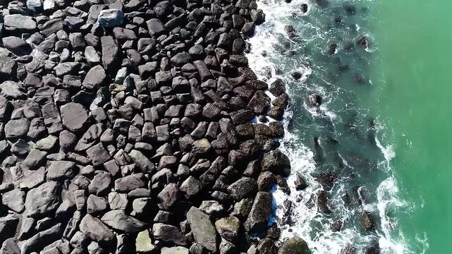 Aerial top view drone shot of ocean waves meeting rocky shoreline with strong contrast and natural texture pattern for abstract background and nature concept