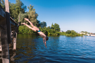 Fototapeta premium Young Boy Diving Headfirst into Calm Lake from Wooden Pier on Sunny Summer Day