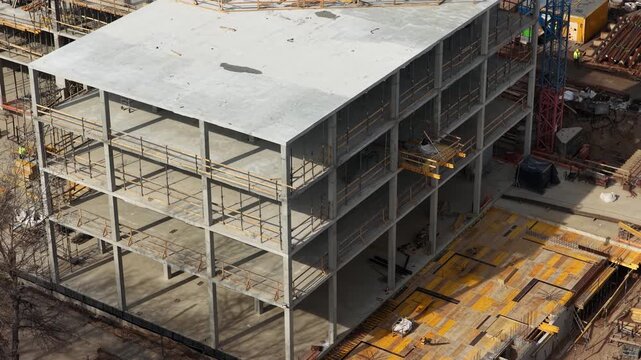 Drone footage capturing a partially completed multi story concrete building with scaffolding, formwork, and materials, highlighting structural progress and active construction environment.
