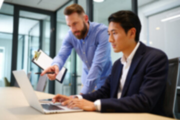 Obraz premium soft focus blurred photo of Professional business colleagues working on laptop in modern office, diverse male coworkers collaborating on corporate project, team mentorship and digital strategy