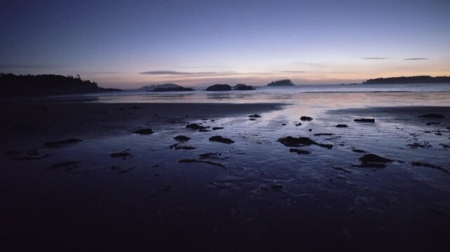 A mesmerizing cinematic motion of an ocean beach at twilight, with the low tide revealing wet sand and distant islands, creating a serene and captivating scene as the sky tr