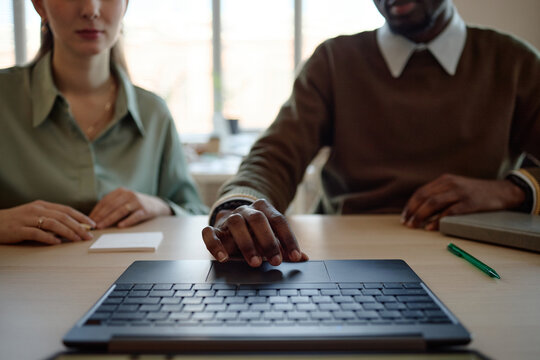 Close up of young adult coworkers reviewing laptop together during office meeting, discussing digital workflow and teamwork. Suitable for business collaboration, training, or hiring content