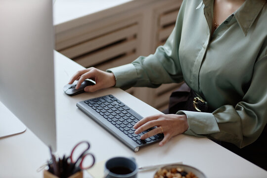 Young adult woman working at desktop computer, typing on keyboard and using mouse at office desk. Suitable for business productivity, administration, remote work, or corporate workflow themes