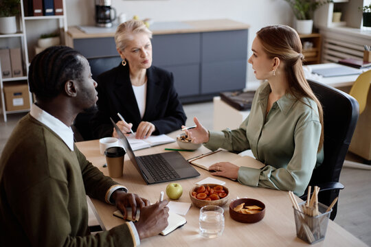 Diverse business team discussing strategy during office meeting, reviewing laptop data and taking notes. Suitable for corporate communication, teamwork, planning, leadership content