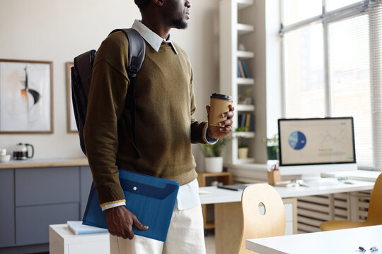 Black young adult man entering office holding coffee, document folder, preparing for workday or meeting. Useful for business commute, onboarding, workplace productivity themes