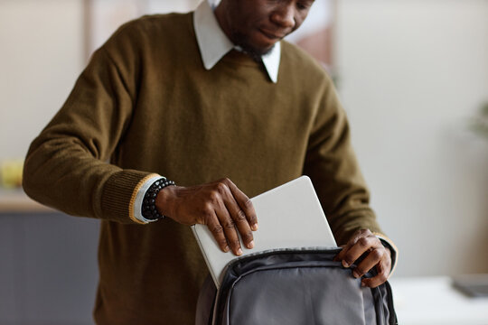 Black young adult man packing laptop into backpack, preparing for commute or remote work transition. Mid shot, fitting business mobility, hybrid work, productivity, or travel campaign use