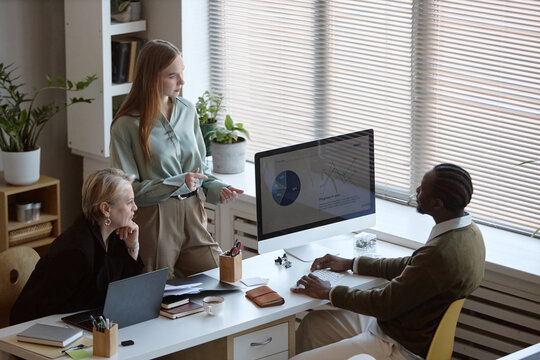 High angle of business team reviewing analytics dashboard on desktop monitor during office meeting. Colleagues discussing strategy and performance metrics for corporate presentation