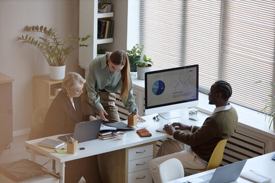 High angle view of diverse business team reviewing sales charts at office desk, discussing strategy and performance. Suitable for corporate planning, teamwork, analytics marketing
