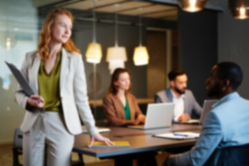 Obraz premium soft focus blurred photo of Confident female leader standing in modern office, professional business team working in background, successful corporate executive in boardroom meeting