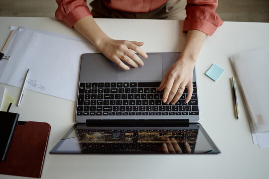 Top-down shot of young adult woman working on laptop at desk, typing and navigating digital tasks for office workflow. Suitable for remote work, productivity, planning, or business content