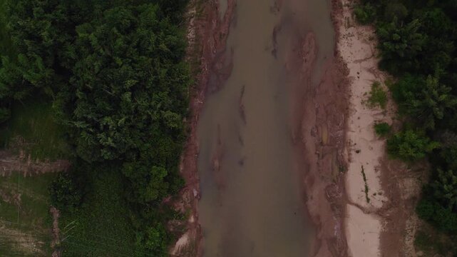 Downward looking perpendicular forward moving view of the Mekong River with green foliage around the river bank.