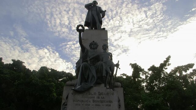 Monument to Juan Pablo Duarte, founding father of the Dominican Republic, with allegorical figures and dramatic cloud-filled sky in Santo Domingo.