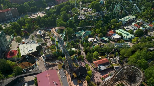 Dramatic aerial parallax pulls back from wooden roller coaster tracks at Liseberg to reveal full amusement park and sweeping Gothenburg city skyline