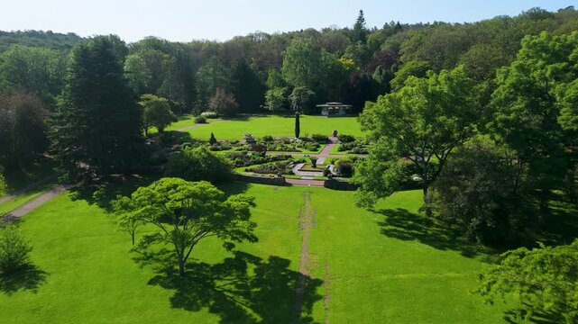 Slow aerial descent over Gothenburg Botanical Garden reveals ornate sunken parterre, central fountain, gazebo pavilion and sweeping manicured lawn surrounded by lush woodland