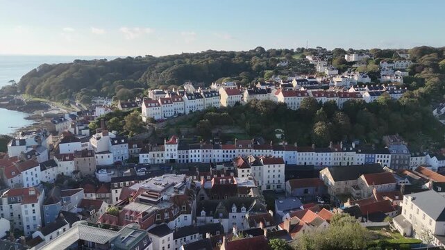 St Peter Port Guernsey Channel Islands high flight over the rooftops of the town flying south towards wooded cliffs of St Martins in late afternoon sun with clear blue sky.